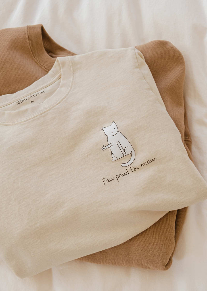 Illustration d'un chat disant "paw paw" sur un sweat-shirt de couleur ivoire.