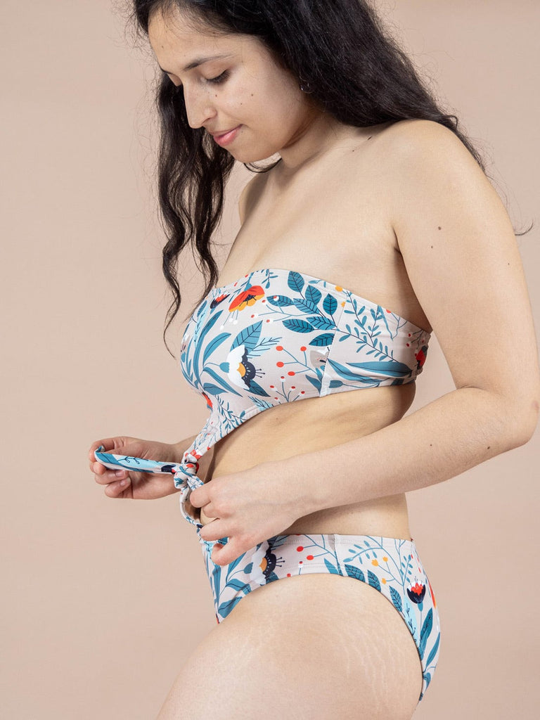 Une femme en bikini bleu à imprimé floral, mettant en valeur le maillot de bain une pièce Wild Flower Knot de la marque Mimi & August.